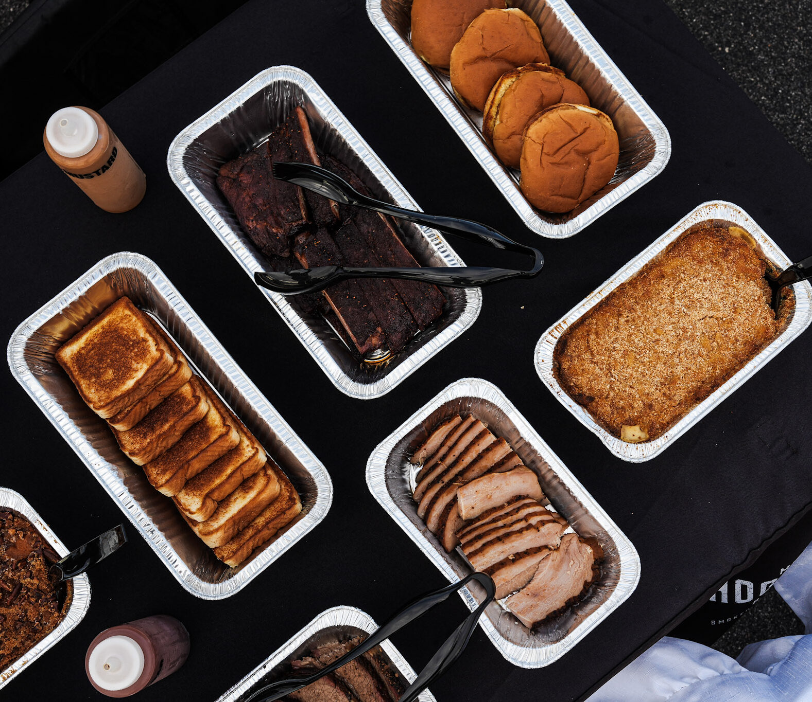 mojo catering close up of tins with ribs, buns, texas toast, turkey, mac n cheese, and sweet potatoes