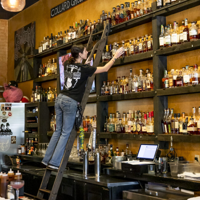 mojo kitchen bartender on a ladder grabbing a bottle of whiskey off the shelf jacksonville beach fl